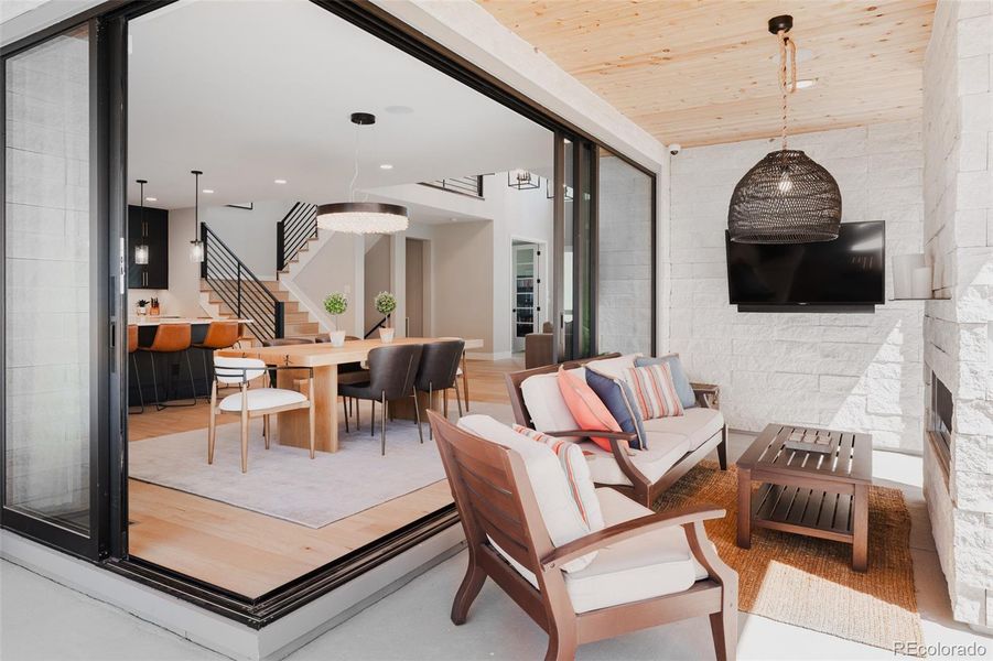 Lustrous light radiates through two sliding walls of glass that converge in the dining room, opening fully to extend the indoor living space outward creating an enchanting relationship to the elevated lanai with fireplace.