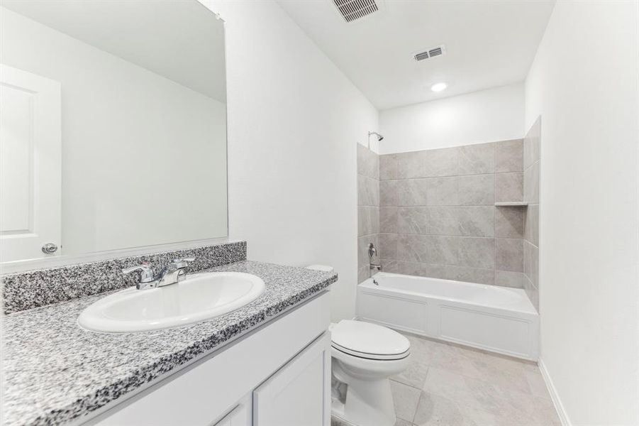 Full bathroom featuring tile patterned flooring, tiled shower / bath combo, toilet, and vanity