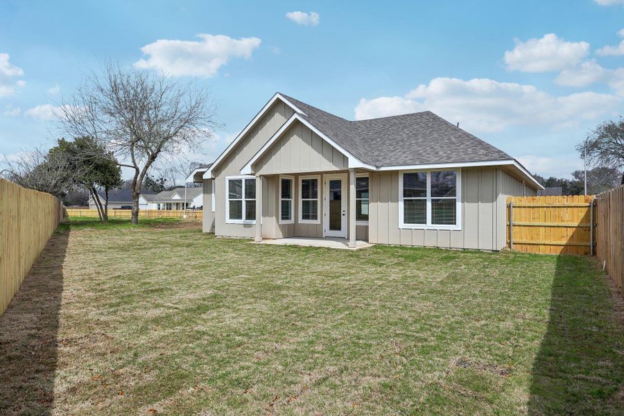 Rear view of house with a lawn, board and batten siding, a shingled roof, and a fenced backyard