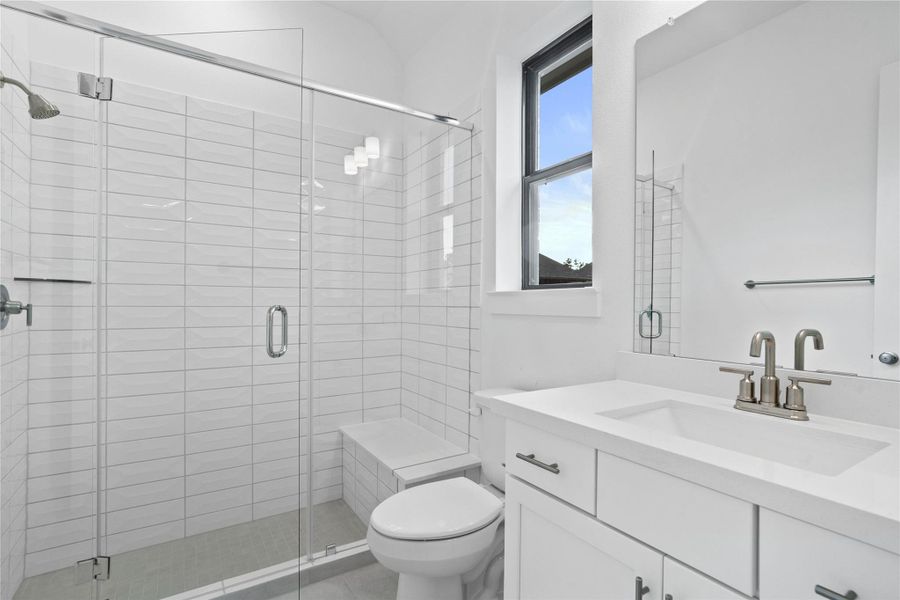 This ensuite secondary bathroom features a modern vanity, large walk-in shower with seat and tile surround, and brushed nickel finishes.