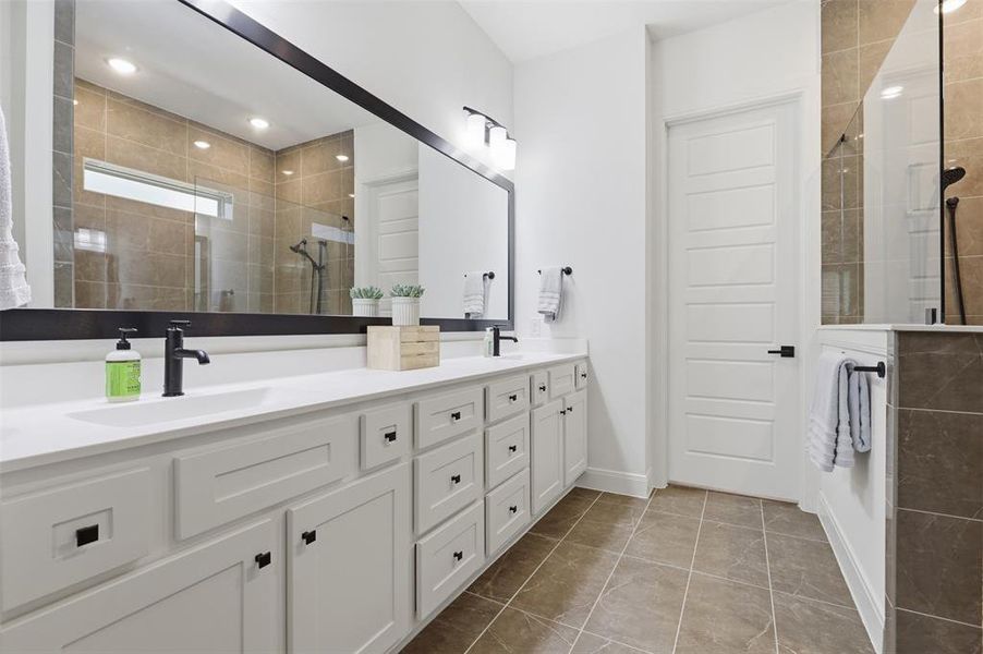 Bathroom featuring a dual vanity with white cabinetry, matte black hardware, and an expansive wall-mounted mirror Bathroom featuring a dual vanity with white cabinetry, matte black hardware, and an expansive wall-mounted mirror
