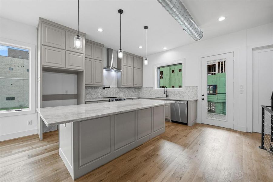 Kitchen featuring gray cabinetry, light stone counters, hanging light fixtures, a center island, and light wood finished floors