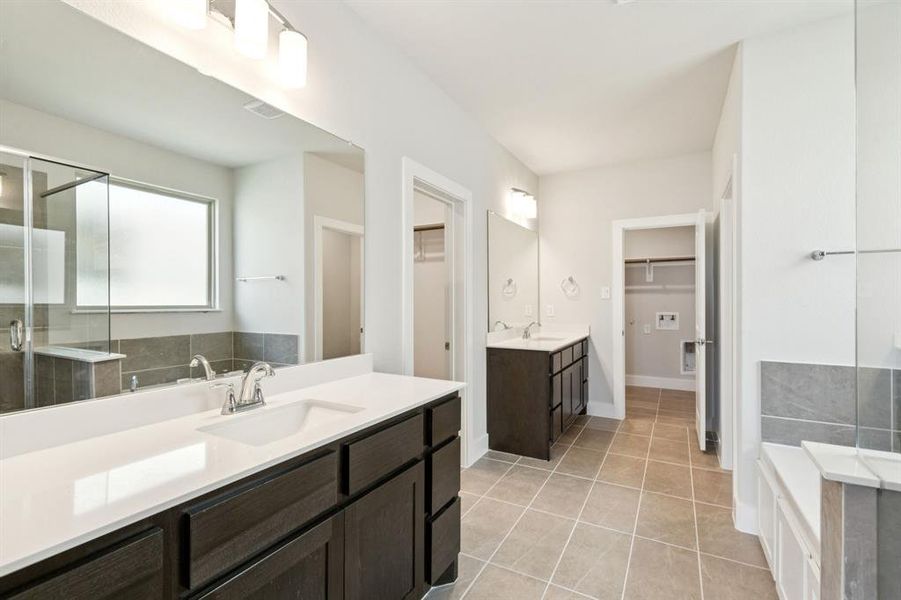 Bathroom with a spacious closet, a shower stall, two vanities, light tile patterned floors, and a garden tub Bathroom with a spacious closet, a shower stall, two vanities, light tile patterned floors, and a garden tub