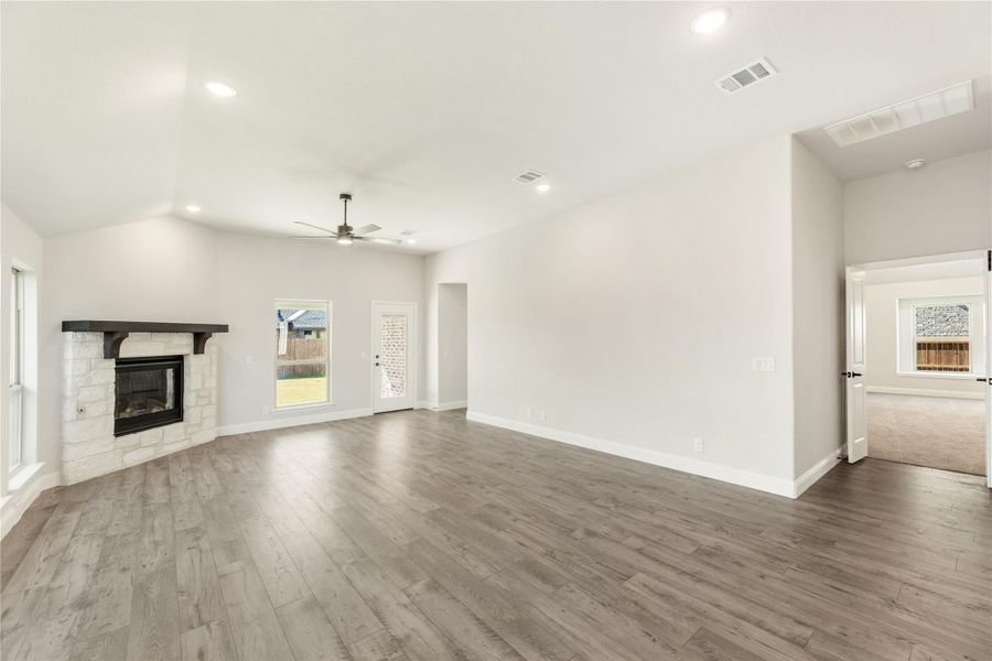 Open living room with stone fireplace, hardwood floors, vaulted ceiling, and ceiling fan