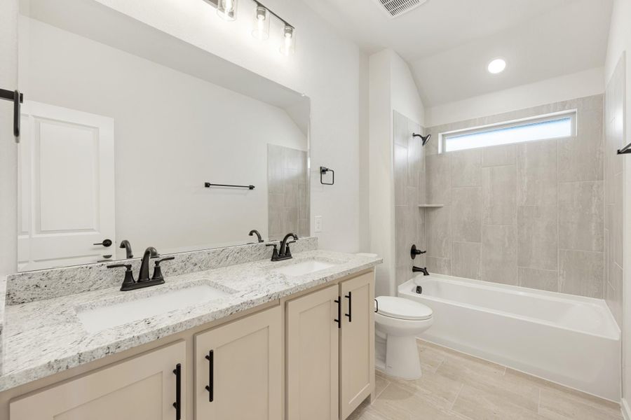 Bathroom with double vanity, granite countertops, and tiled tub-shower combo with small window above
