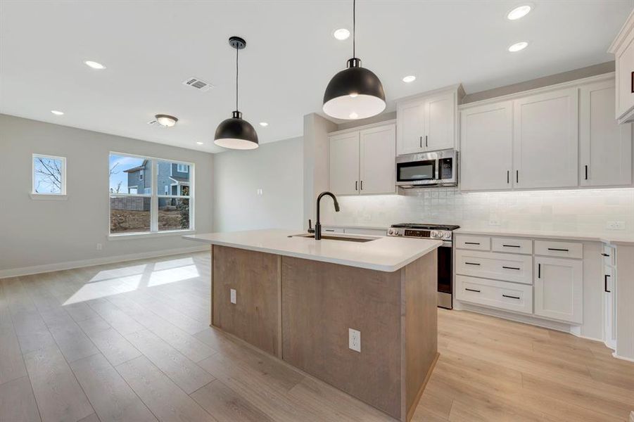 Dual tone kitchen featuring stainless steel appliances, an island with sink, decorative light fixtures, backsplash, and open floor plan