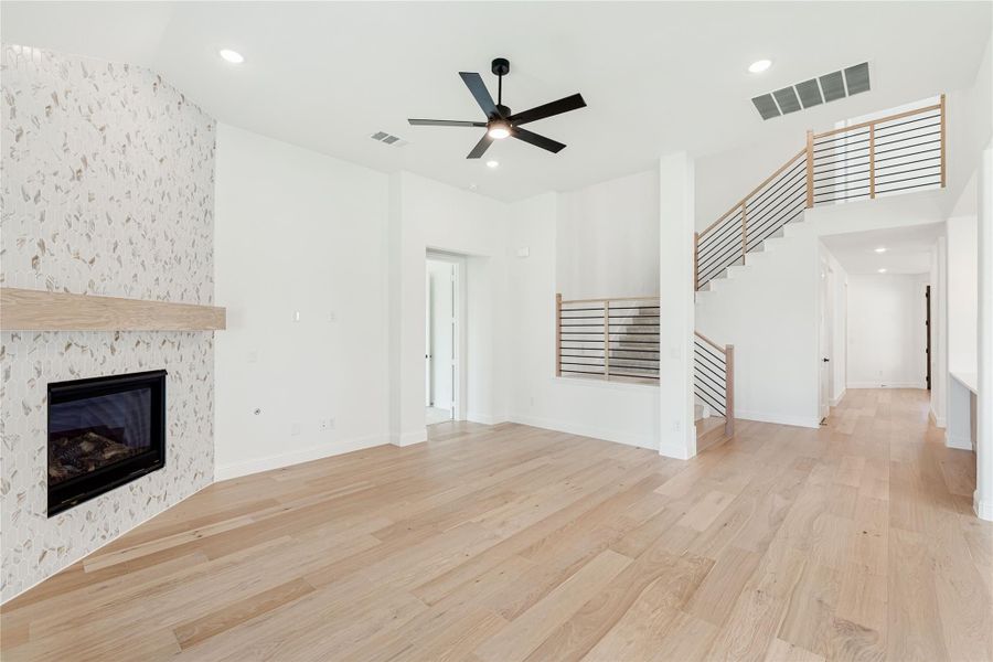Open living room with tile fireplace, hardwood floors, ceiling fan, and open staircase with metal railing Open living room with tile fireplace, hardwood floors, ceiling fan, and open staircase with metal railing