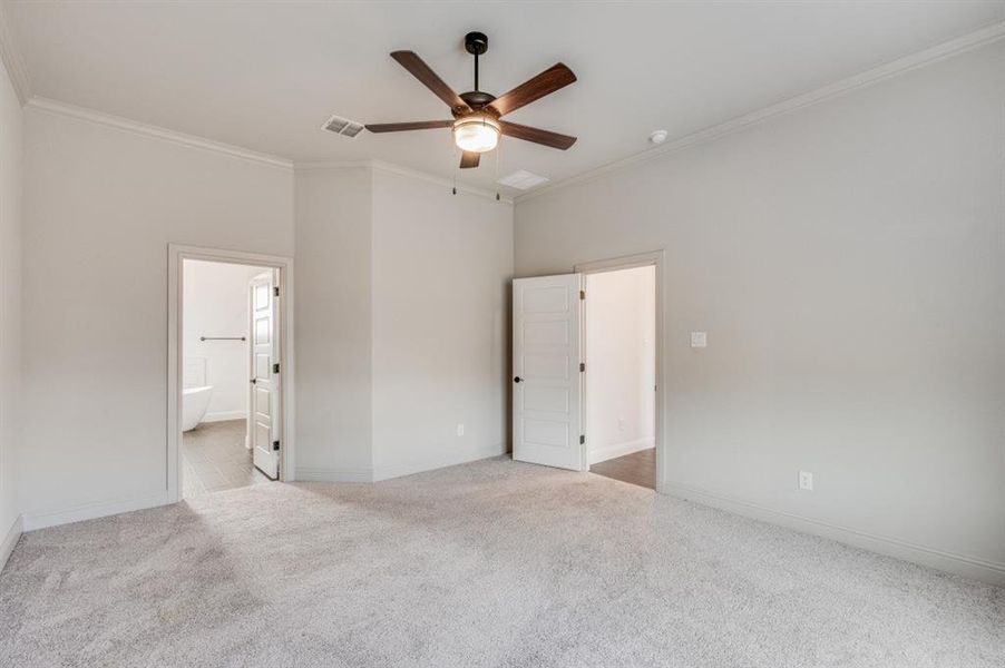 Unfurnished bedroom with connected bathroom, light colored carpet, ceiling fan, and crown molding