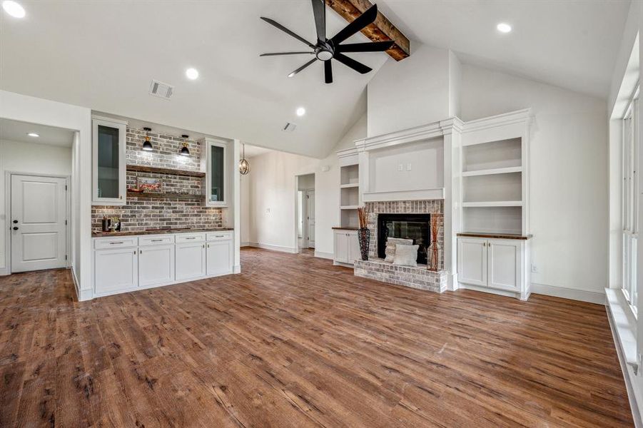 Unfurnished living room featuring beam ceiling, a brick fireplace, hardwood / wood-style floors, and ceiling fan