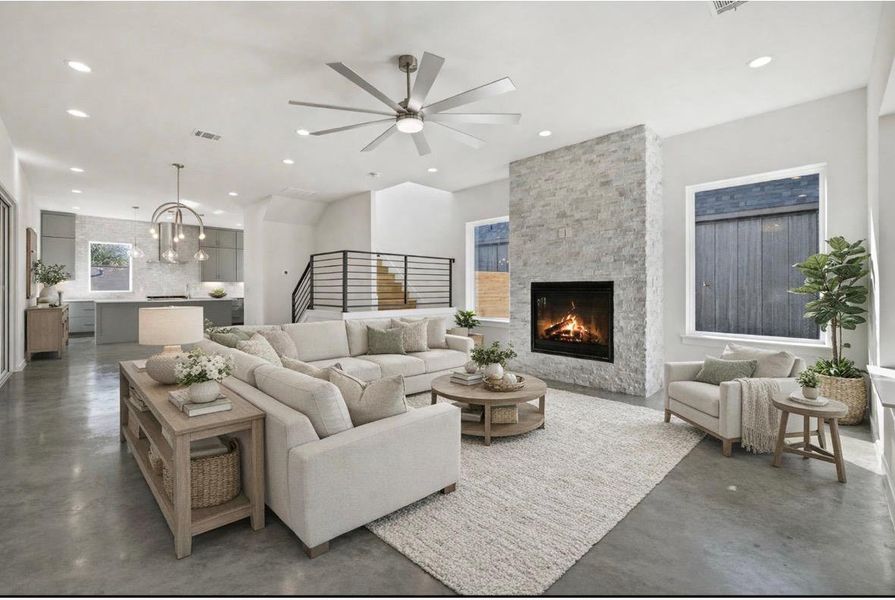 Living room featuring concrete flooring, a fireplace, a ceiling fan, and suspended lighting