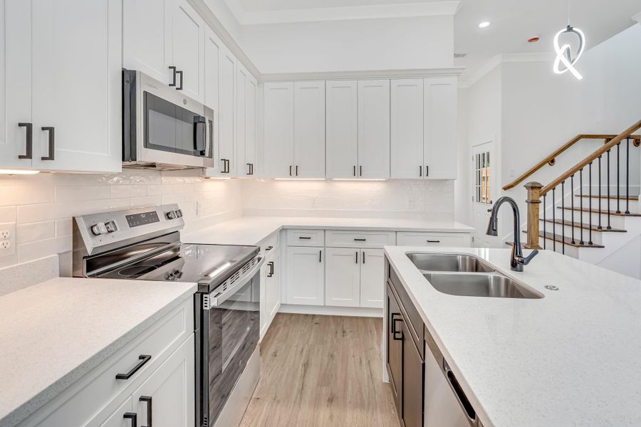Modern kitchen featuring quartz countertops, white soft-closing shaker cabinets with black hardware, stainless steel appliances, and a spacious waterfall island with farmhouse-style sink.