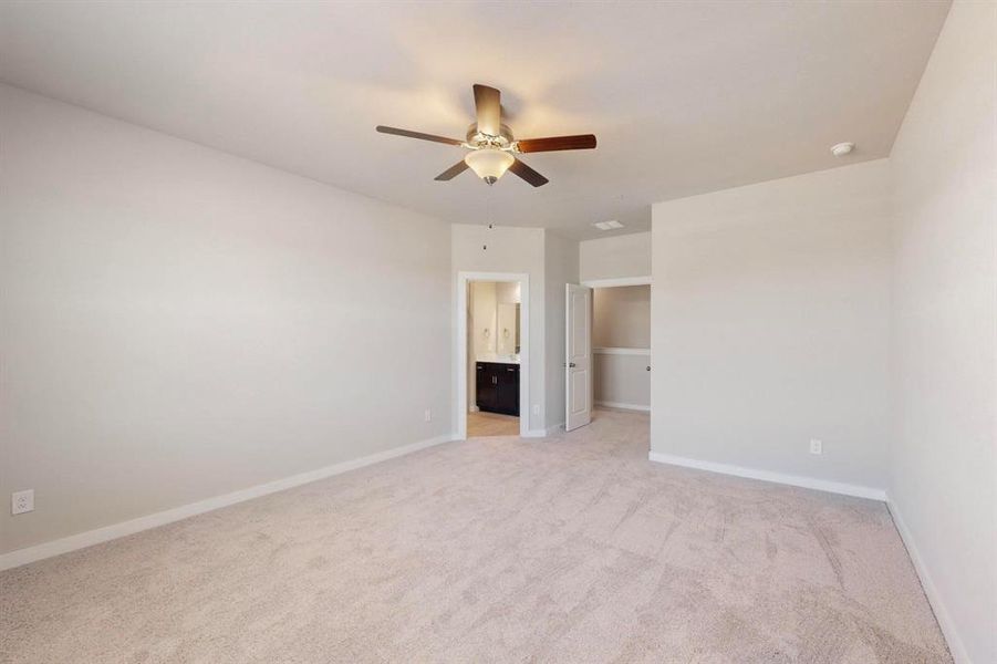 Unfurnished bedroom featuring a spacious closet, light carpet, a ceiling fan, and ensuite bath