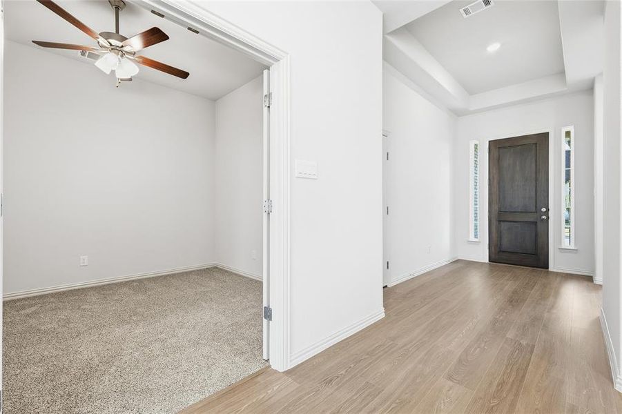 Entryway featuring ceiling fan, light wood-style flooring, a tray ceiling, and light colored carpet Entryway featuring ceiling fan, light wood-style flooring, a tray ceiling, and light colored carpet