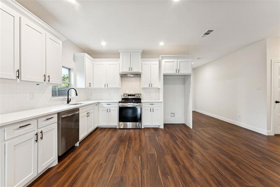 Kitchen with white cabinetry, stainless steel appliances, dark wood-style flooring, recessed lighting, and backsplash