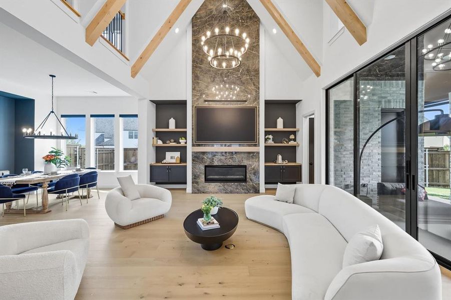 Living room featuring a chandelier, a black stone fireplace, light hardwood flooring, built in shelves, and a towering ceiling Living room featuring a chandelier, a black stone fireplace, light hardwood flooring, built in shelves, and a towering ceiling