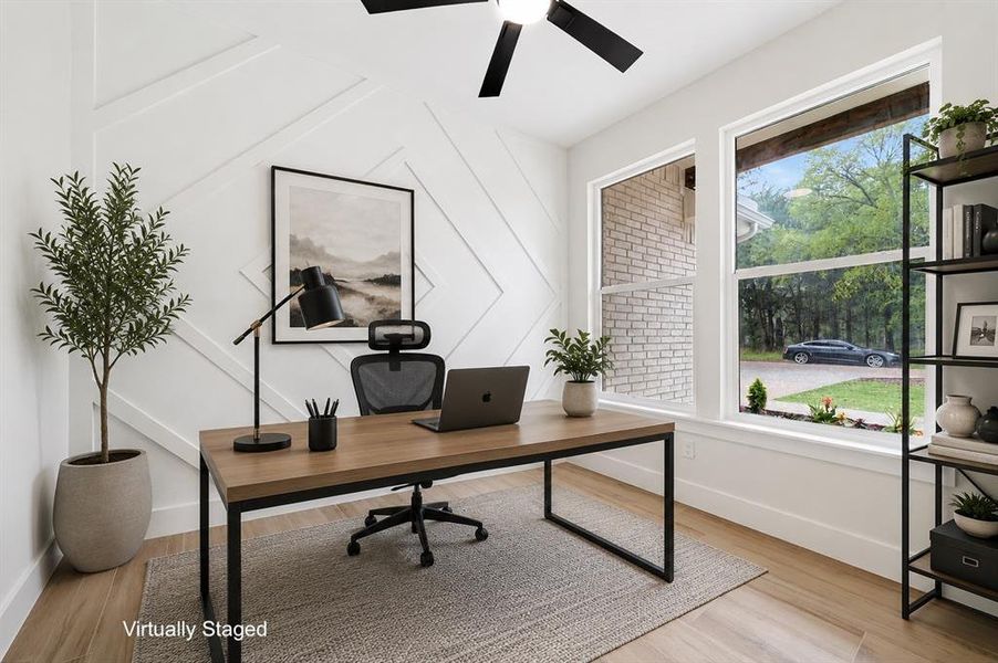 Bright room featuring decorative wainscoting, multiple windows with exterior views, wood-finish flooring, and a ceiling fan Bright room featuring decorative wainscoting, multiple windows with exterior views, wood-finish flooring, and a ceiling fan