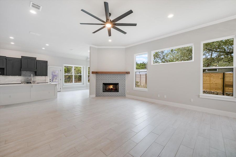 Unfurnished living room featuring visible vents, baseboards, light wood finished floors, a tiled fireplace, and crown molding