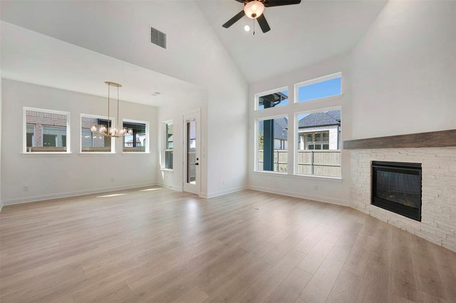 Unfurnished living room featuring vaulted ceiling, a fireplace, a ceiling fan, suspended lighting, and light wood-type flooring