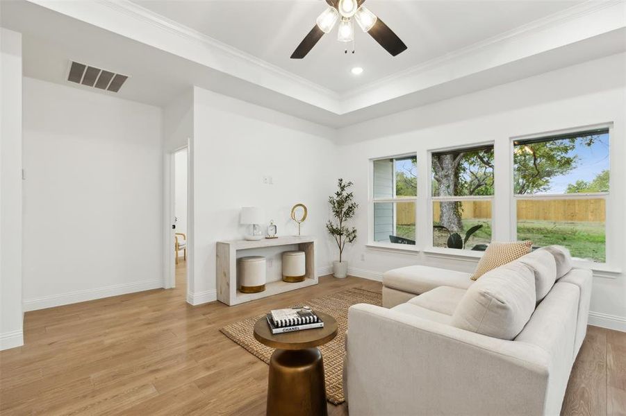 Living room featuring ceiling fan, a raised ceiling, light wood-type flooring, and crown molding