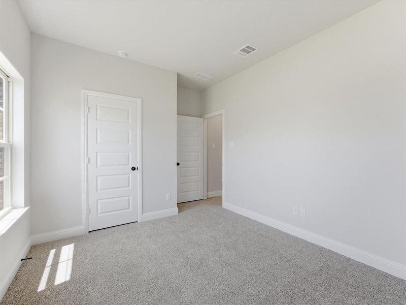 Spacious room featuring light gray carpeting, neutral wall paint, white trim, and a multi-pane window Spacious room featuring light gray carpeting, neutral wall paint, white trim, and a multi-pane window