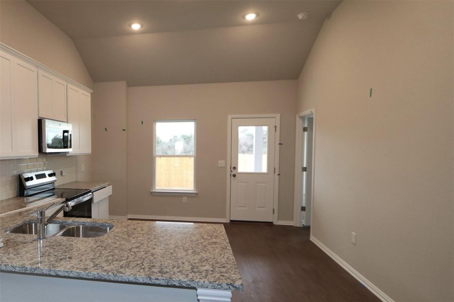 Kitchen with sink, light stone counters, white cabinets, and appliances with stainless steel finishes