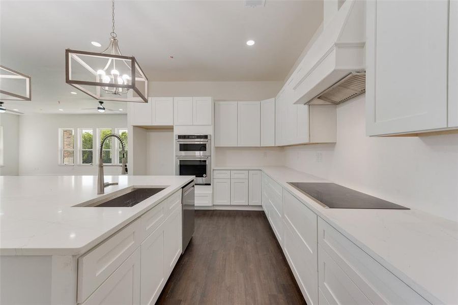 Kitchen with custom exhaust hood, white cabinetry, appliances with stainless steel finishes, dark hardwood / wood-style floors, and light stone countertops