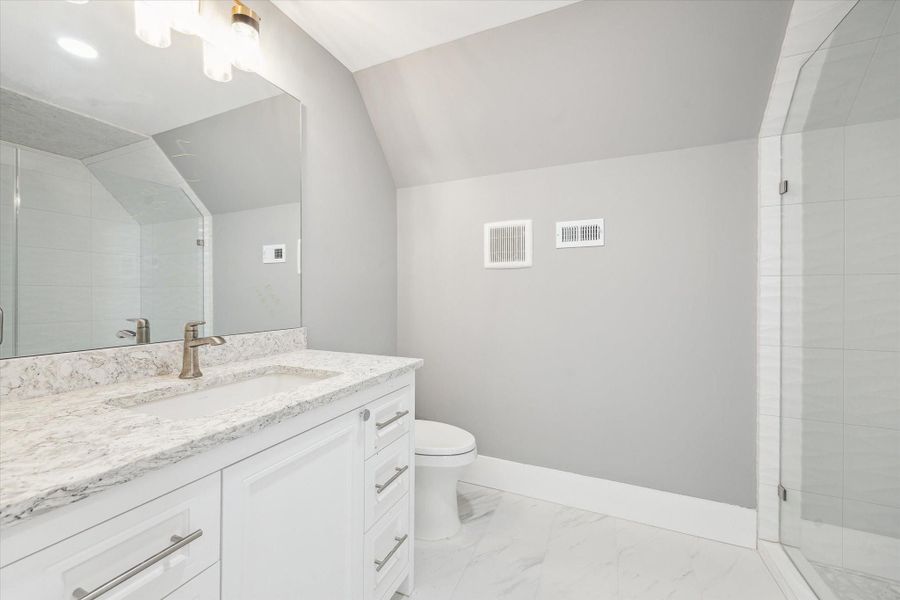 This bathroom features a modern design with a sleek white vanity, marble countertop, large mirror, and a spacious glass-enclosed shower. The neutral gray walls and bright lighting create a fresh and inviting atmosphere.