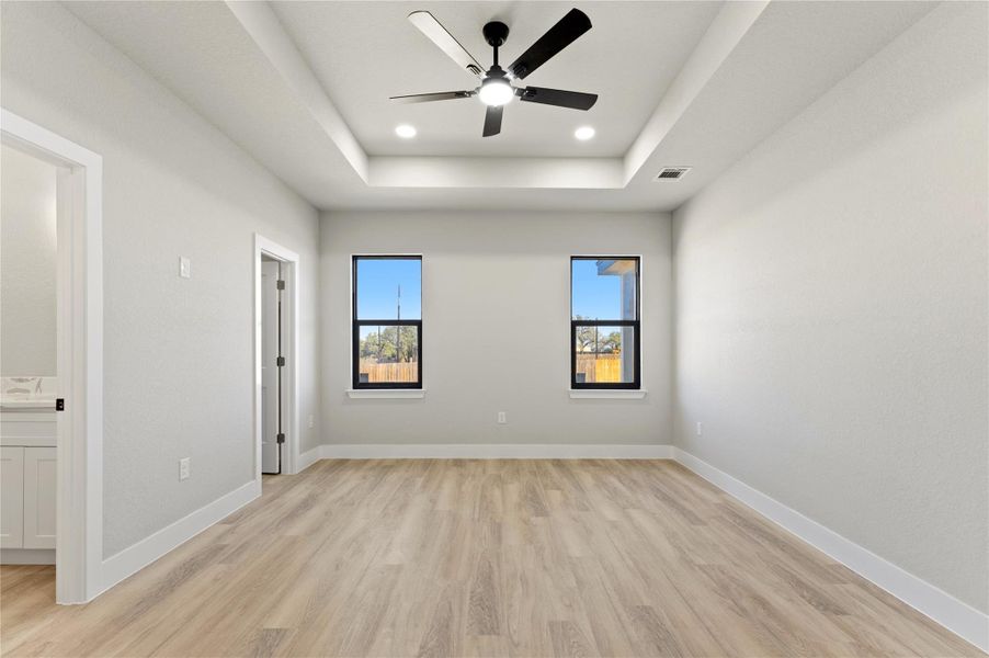 Unfurnished bedroom featuring light wood-style floors, ceiling fan, recessed lighting, a tray ceiling, and connected bathroom