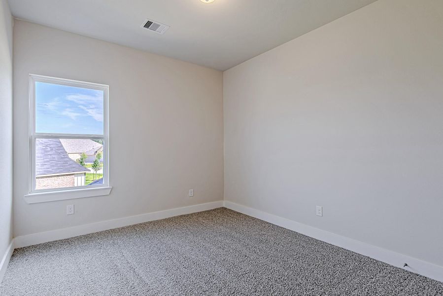 A cozy secondary bedroom featuring soft neutral tones, plush carpeting, and a large window that frames the sky beautifully.