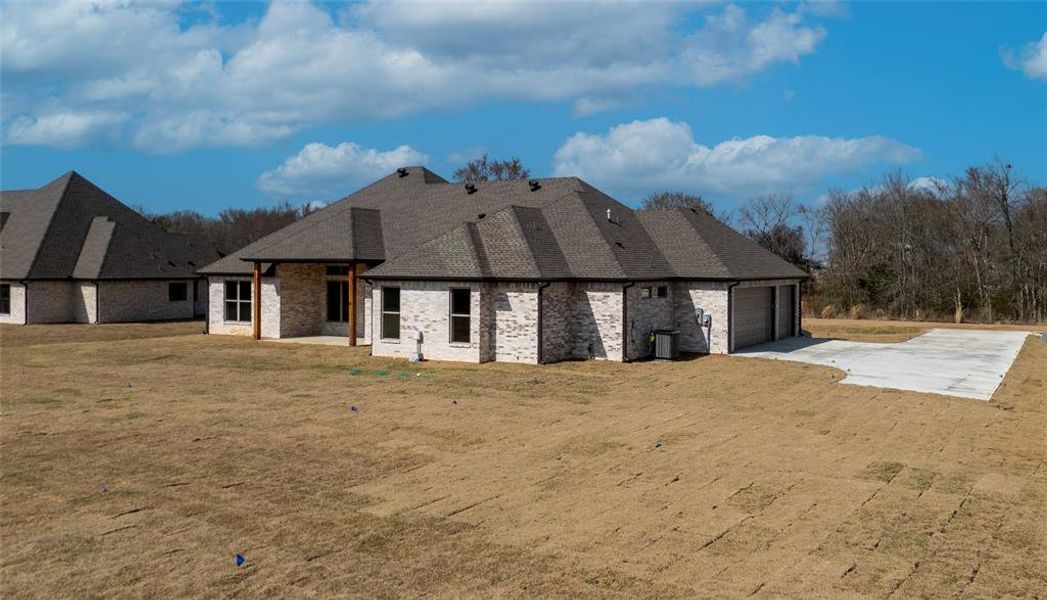 Rear view of property featuring a patio area, a lawn, concrete driveway, a garage, and brick siding