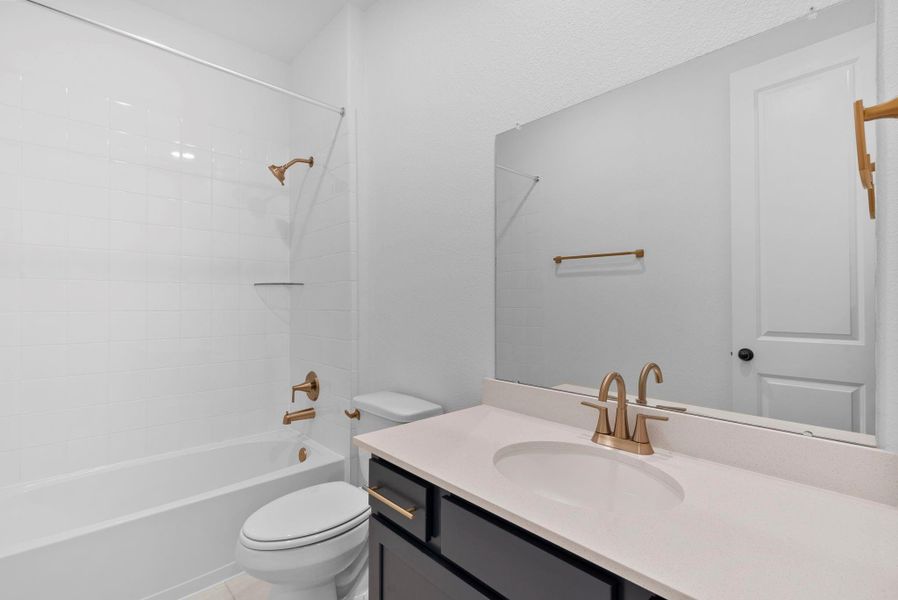 Inviting secondary bath featuring the AW Collection Sapphire with navy cabinetry and light countertops with brass fixtures and a shower/tub combo.