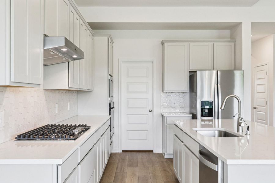 Kitchen featuring backsplash, stainless steel appliances, light stone counters, a kitchen island with sink, and light wood-style floors Kitchen featuring backsplash, stainless steel appliances, light stone counters, a kitchen island with sink, and light wood-style floors
