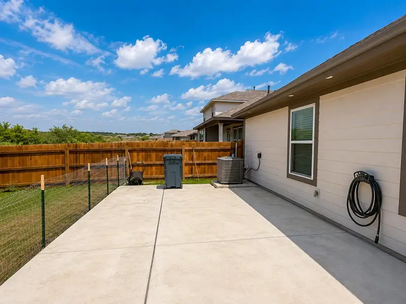 A spacious concrete patio awaits outdoor enjoyment, bordered by a wooden privacy fence under a clear sky. A spacious concrete patio awaits outdoor enjoyment, bordered by a wooden privacy fence under a clear sky.