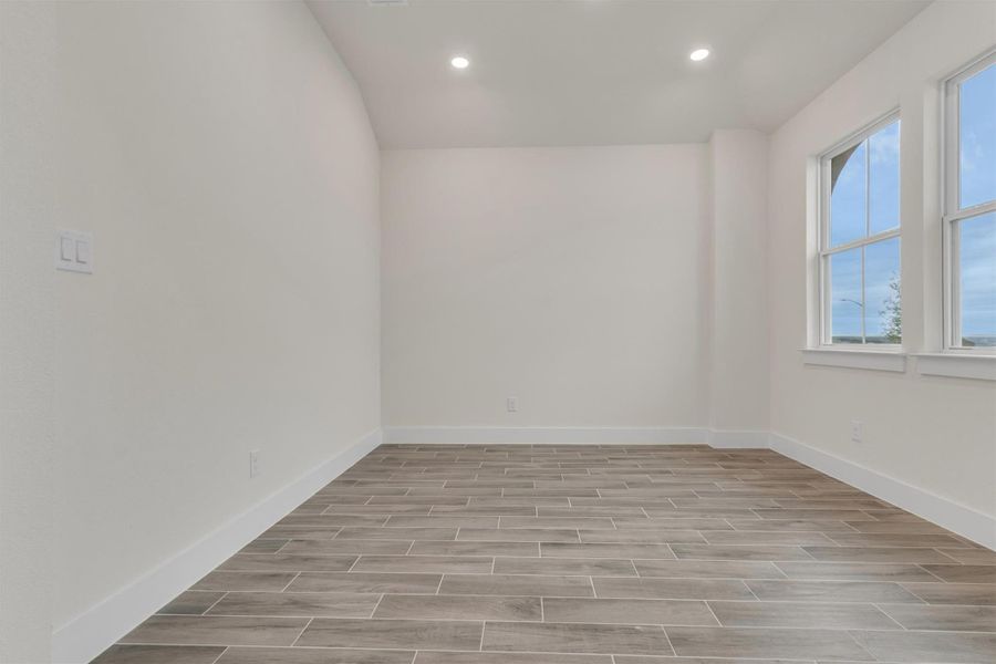 Recessed lighting illuminates this versatile space, featuring durable wood-look tile flooring and ample natural light.