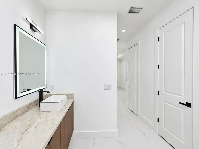 Vanity featuring stone-finish countertop, wood-finish cabinetry, rectangular vessel sink, matte black faucet, and an integrated LED-lighted mirror