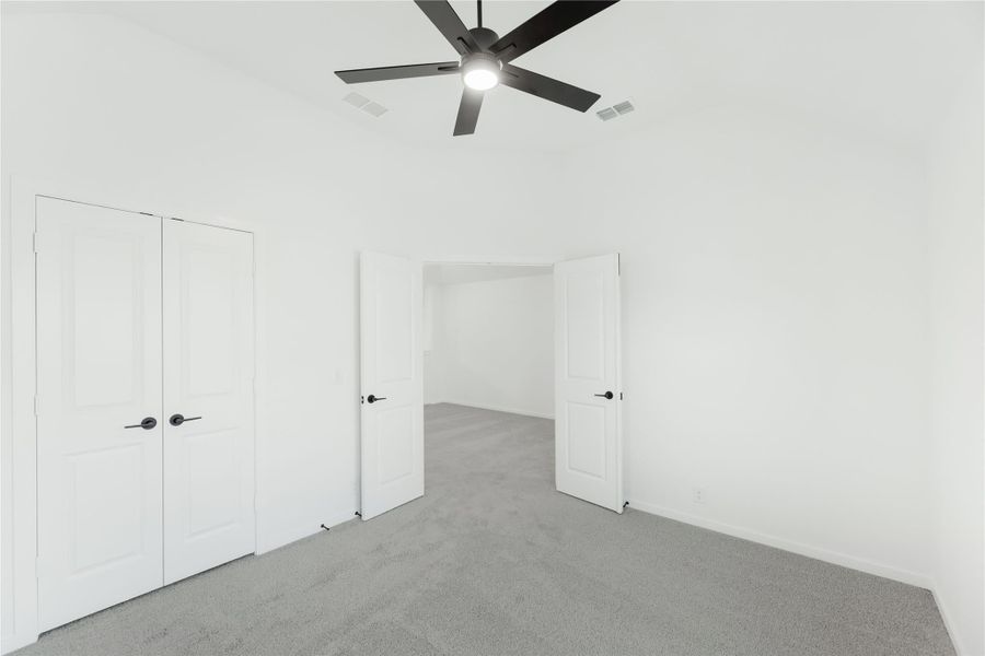 Empty bedroom with gray carpet, white walls, closet doors, and black ceiling fan Empty bedroom with gray carpet, white walls, closet doors, and black ceiling fan