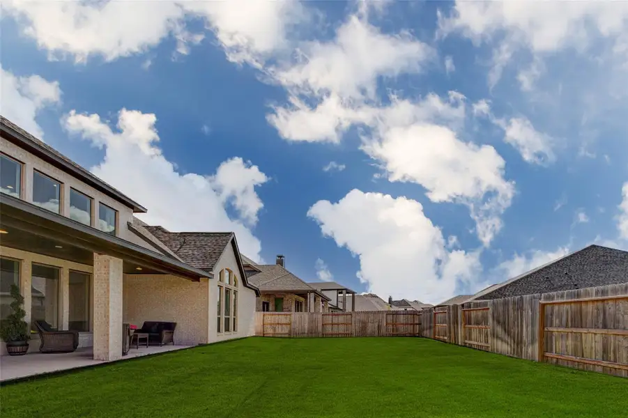 Spacious backyard with a well-maintained lawn, bordered by a wooden fence. The home features a covered patio area, large windows, and a brick exterior. The sky is clear with scattered clouds, creating a bright and inviting atmosphere. Spacious backyard with a well-maintained lawn, bordered by a wooden fence. The home features a covered patio area, large windows, and a brick exterior. The sky is clear with scattered clouds, creating a bright and inviting atmosphere.