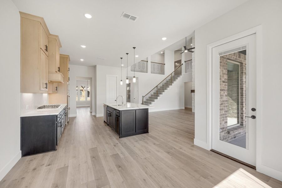 Open-concept kitchen with dark island, light wood floors, and staircase visible in background Open-concept kitchen with dark island, light wood floors, and staircase visible in background