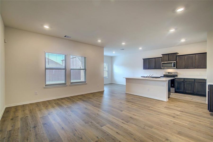 Kitchen with a kitchen island with sink, stainless steel appliances, light wood finished floors, open floor plan, and recessed lighting