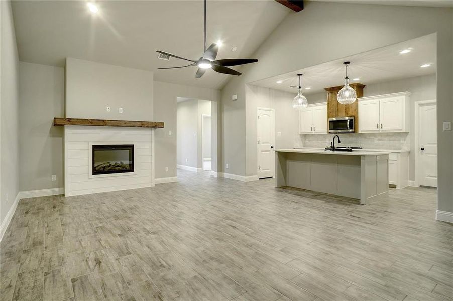 Unfurnished living room featuring light wood-style floors, a tile fireplace, high vaulted ceiling, recessed lighting, and beamed ceiling