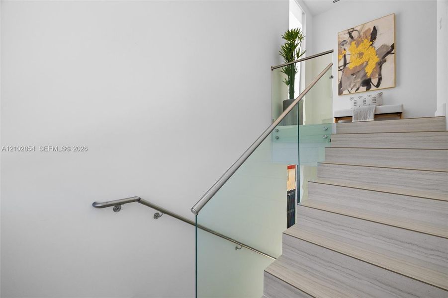 Staircase featuring wood-finish treads, glass panel railing, and a brushed metal handrail