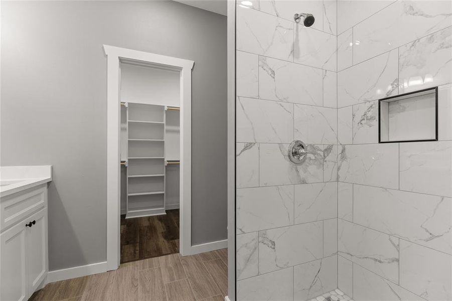 Full bathroom with vanity, a tile shower, wood finish floors, and a walk in closet