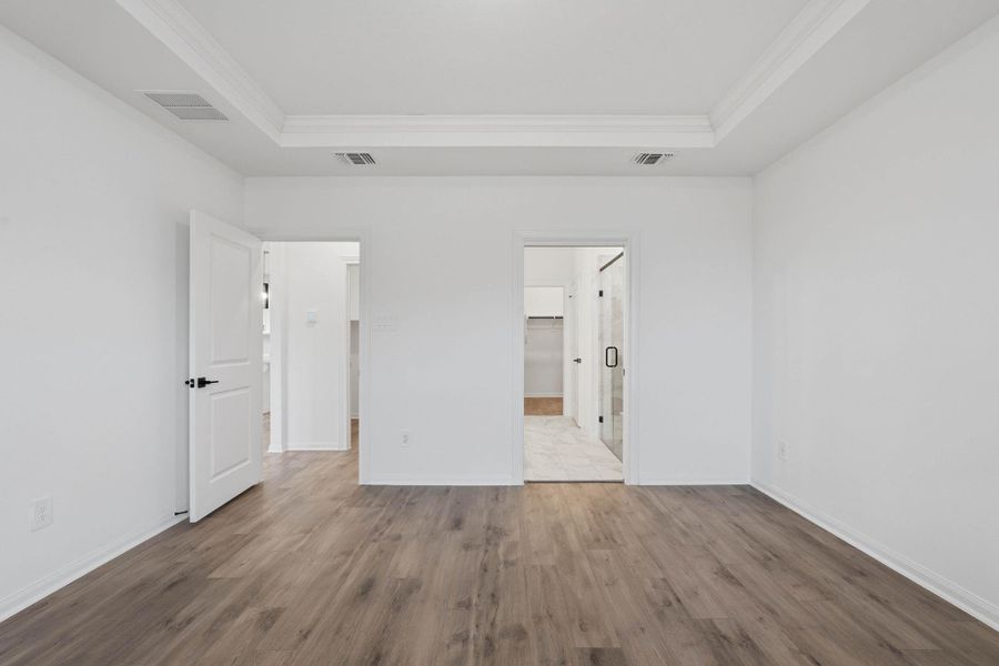 The primary suite feels spacious and refined, featuring crown molding, rich warm floors and easy access to a walk-in closet and spa-like bathroom.
