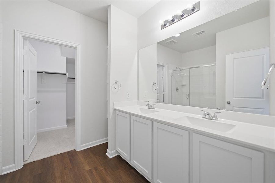 Double vanity with undermount sinks and white cabinetry, expansive mirror, wood-finish flooring, and a walk-in closet with built-in shelving