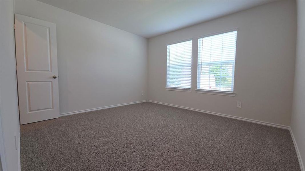 Spacious room featuring neutral wall tones, gray carpeting, dual windows with blinds, and white trim Spacious room featuring neutral wall tones, gray carpeting, dual windows with blinds, and white trim