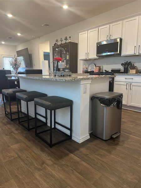 Kitchen featuring white cabinetry, stainless steel microwave, light stone countertops, a kitchen bar, and recessed lighting