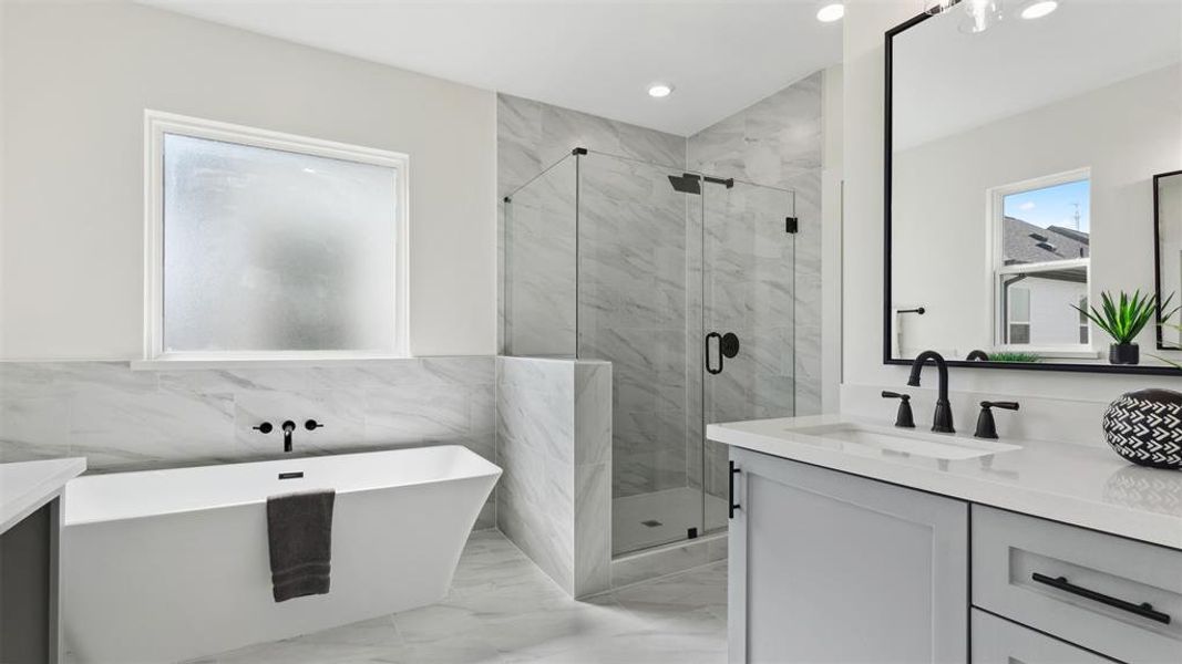 This modern bathroom features a sleek design with a freestanding bathtub, a glass-enclosed shower, and stylish fixtures. The space is brightened by natural light from large windows and has elegant marble-like tiles for a luxurious feel.