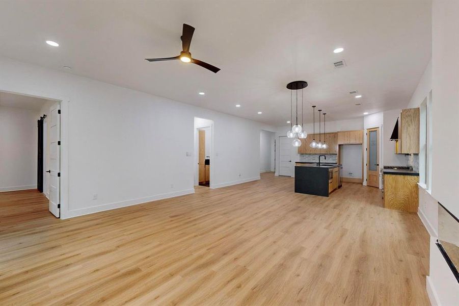 Expansive open-concept living area featuring light wood-finish flooring, recessed lighting, and a contemporary ceiling fan Expansive open-concept living area featuring light wood-finish flooring, recessed lighting, and a contemporary ceiling fan