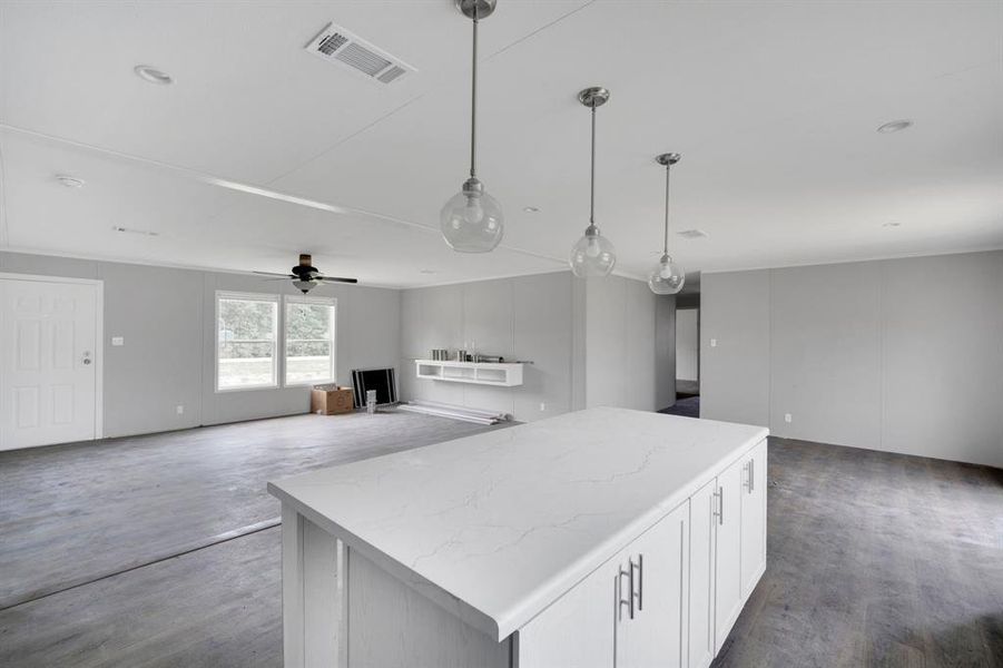 Kitchen island featuring a light-toned countertop, white cabinetry with silver-toned hardware, and three suspended clear glass pendant lights
