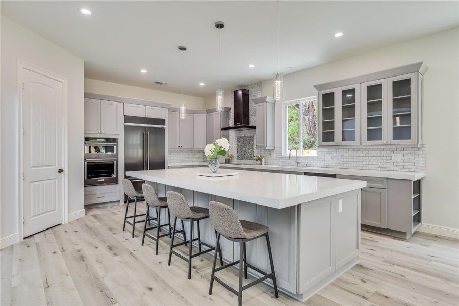 Kitchen featuring a large island, high end fridge, a breakfast bar area, hanging light fixtures, and wall chimney range hood